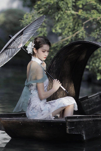 一个打扮成仙女的年轻女子撑着伞坐在水中的小船上