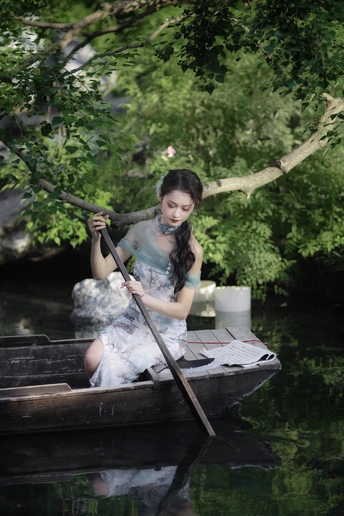 一位身穿白色衣服的年轻女士坐在一条沿着河流划船的船上