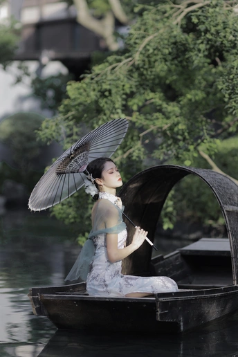 一个穿着连衣裙、打着黑色雨伞的年轻女子坐在水面上的小船上