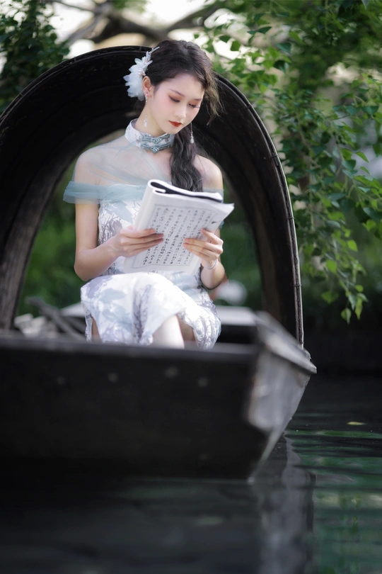 一个穿着连衣裙的年轻女子坐在河边的贡多拉里看书