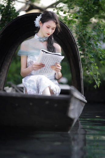 一个穿着连衣裙的年轻女子坐在河边的贡多拉里看书