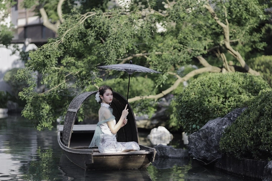 一个撑着伞的女人坐在池塘里的小船上