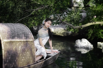 坐在河里或小溪里的小船上的穿着连衣裙的年轻女子