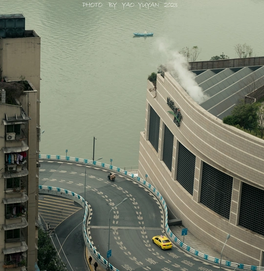 一辆黄色出租车沿着河边街道行驶 两侧都是高楼大厦。