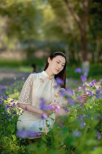 一位穿着白色连衣裙的美丽年轻女子坐在紫花丛中