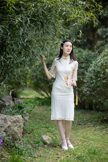 一位穿着白色连衣裙的年轻女子站在一棵树下 手里拿着一把雨伞。