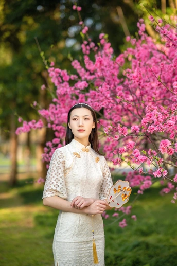 穿着传统服装的年轻女子抱着一只蝴蝶站在一个开满树木和粉红色花朵的公园里。