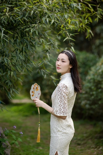 一位穿着白色连衣裙的美丽年轻女子站在一个有树木的花园中 手里拿着一把阳伞。