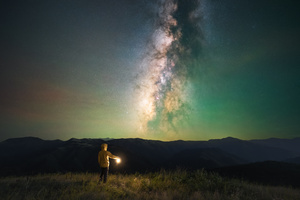 一个人拿着手电筒仰望星空 远处有星星和山脉。