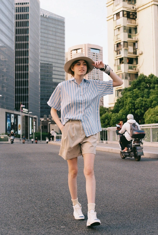 一个穿着衬衫和帽子的人在街上站立 背景中有一辆摩托车驶过。