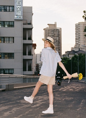 一位穿着连衣裙和帽子 拿着网球拍 穿越街道的年轻女子