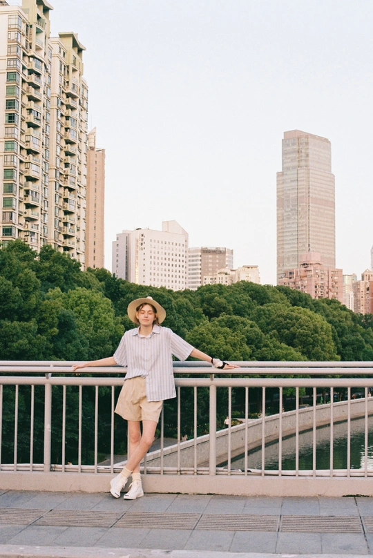 一位戴帽子的人在河上的桥上倚靠在栏杆上 背景是一座城市。