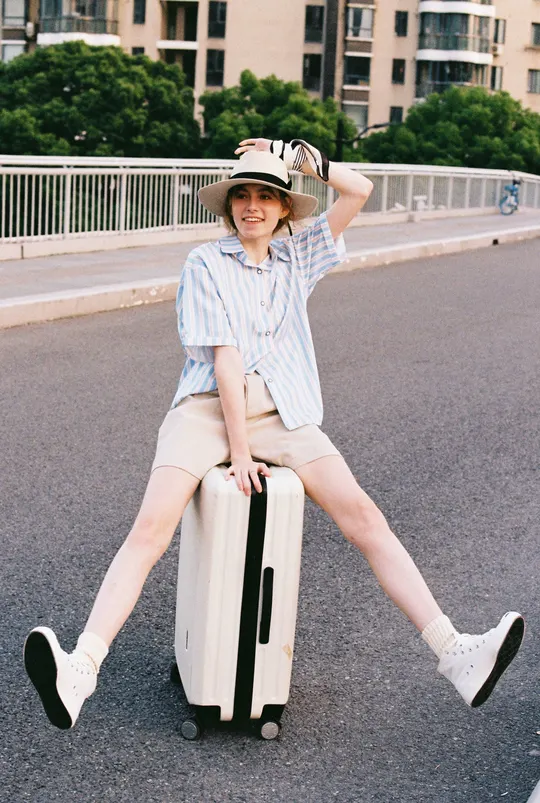 一个戴帽子坐在行李箱上的年轻女子在马路中央