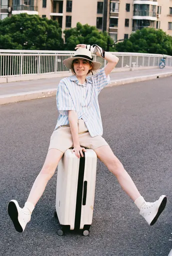 一个戴帽子坐在行李箱上的年轻女子在马路中央