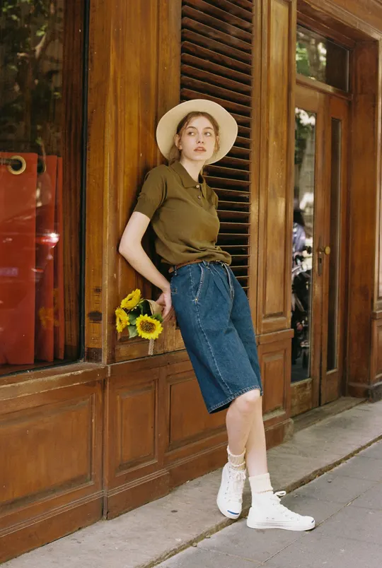 一位穿着棕色衬衫和帽子站在黄色花朵窗户前的年轻女子