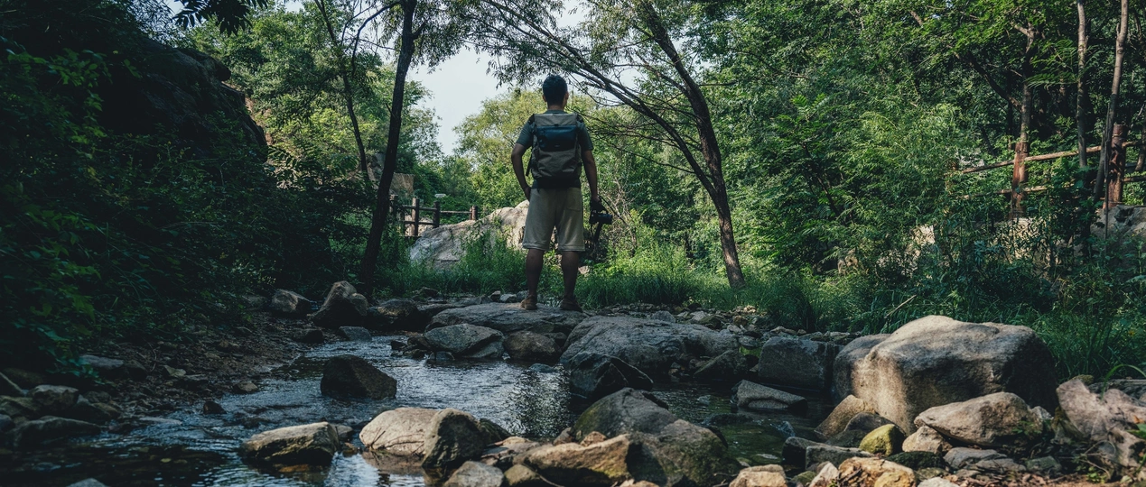 一个背着背包的男人站在一条溪流中的岩石上