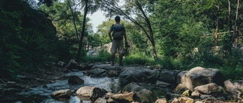 一个背着背包的男人站在一条溪流中的岩石上