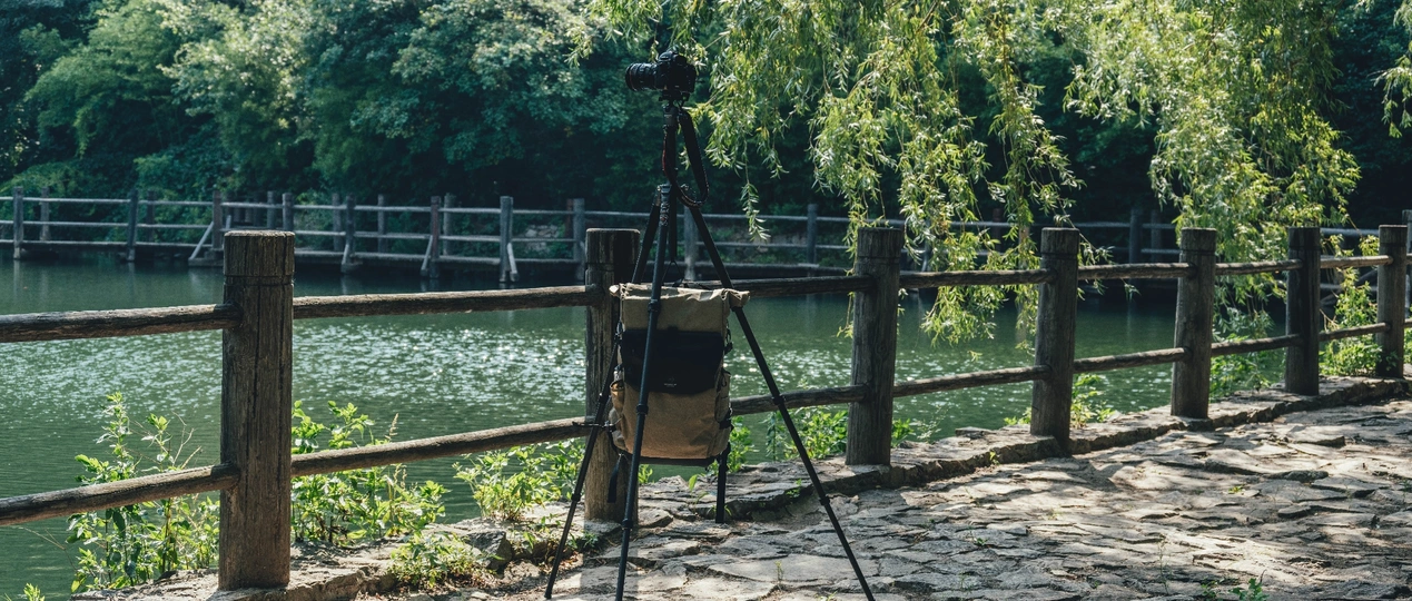 在河边或湖边的一根木栅栏前 有一架三脚架上的相机。