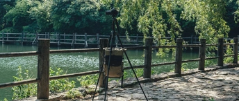 在河边或湖边的一根木栅栏前 有一架三脚架上的相机。