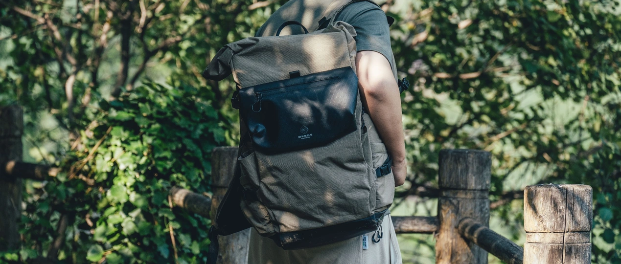 一个背着黑色背包的男人 拿着黑色袋子 在森林里沿着木桥走。