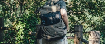 一个背着黑色背包的男人 拿着黑色袋子 在森林里沿着木桥走。