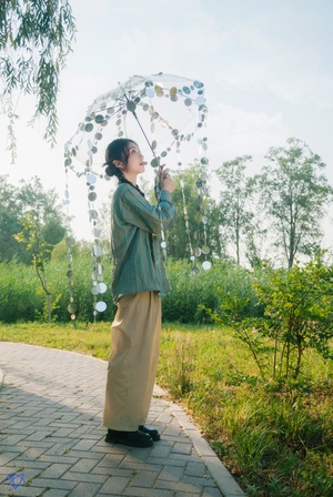 一位年轻女子手持雨伞站在茂密的绿色草地上