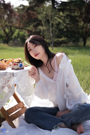 一个年轻女子坐在公园的白毛毯上 为拍照摆姿势 蛋糕和纸杯蛋糕放在草地上。