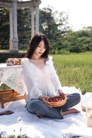 一个穿着白衬衫的年轻女子坐在公园的草地上 带着一个樱桃篮和一个草莓草篮 准备野餐。