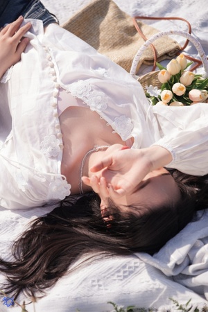 一个穿着白裙子的年轻女子躺在沙滩上 手里拿着花。