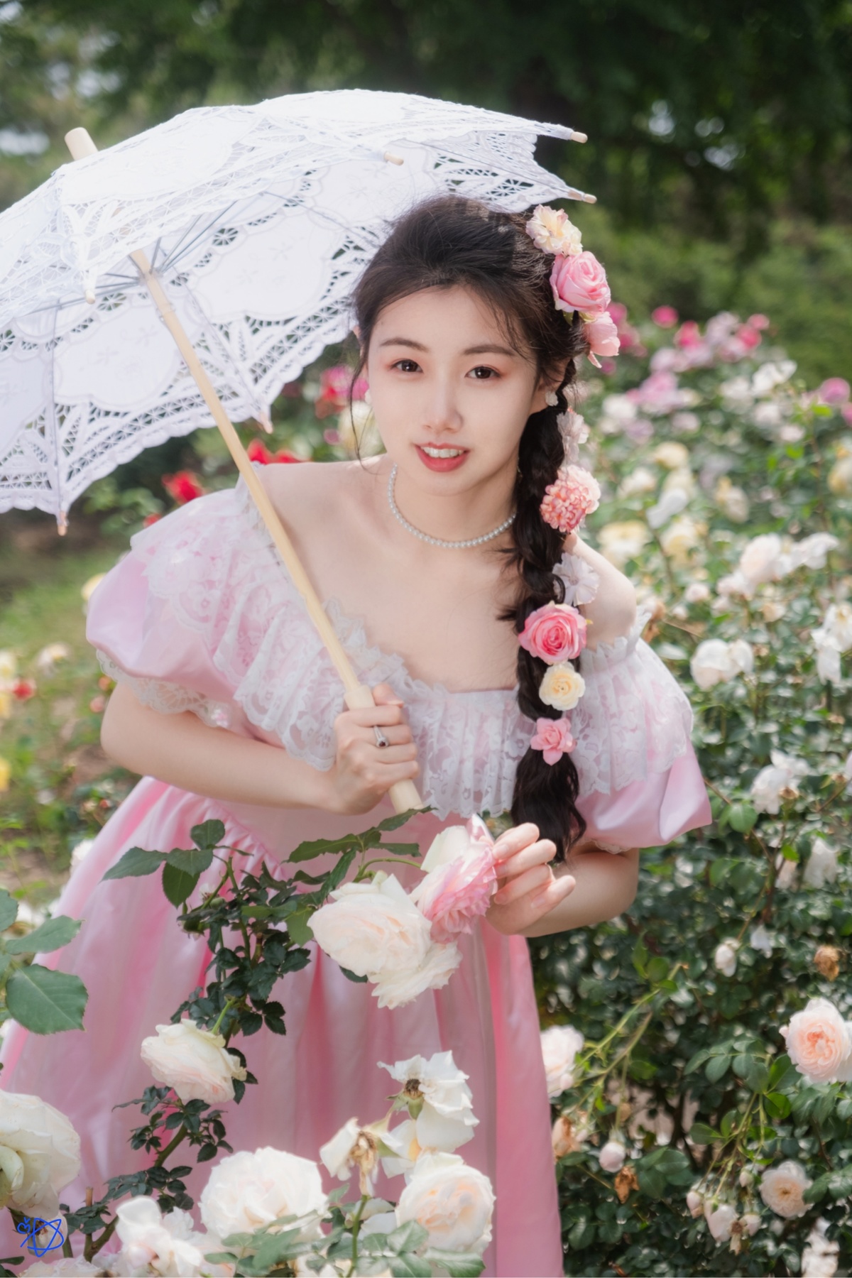 一位穿着粉红色连衣裙的年轻女子 手持白色雨伞 在玫瑰花丛中摆姿势。