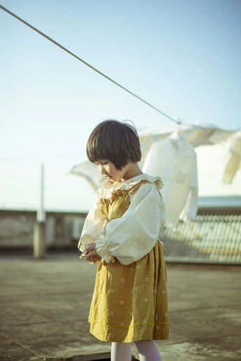 一个穿着黄色连衣裙的小女孩站在屋顶上 另一个小孩在一旁看着