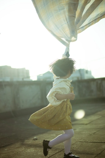 一个穿着黄色连衣裙的小女孩在屋顶上跳 而一个小孩在她身后拉着窗帘
