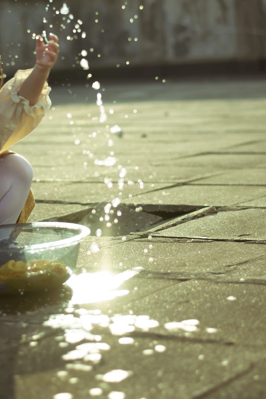 一个小女孩坐在地板上玩喷泉里的一小碗水
