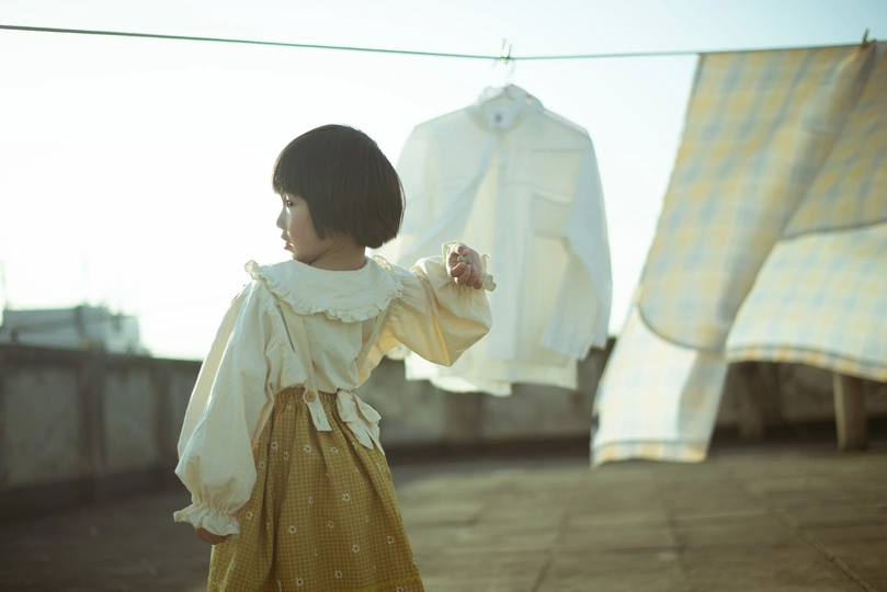 一个穿着黄色连衣裙的年轻女孩站在屋顶上 身后的晾衣绳上挂着要洗的衣服