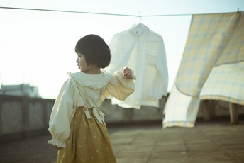 一个穿着黄色连衣裙的年轻女孩站在屋顶上 身后的晾衣绳上挂着要洗的衣服