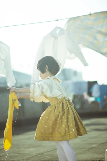 一个穿着黄色连衣裙的小女孩拿着一把小伞站在晾衣绳上