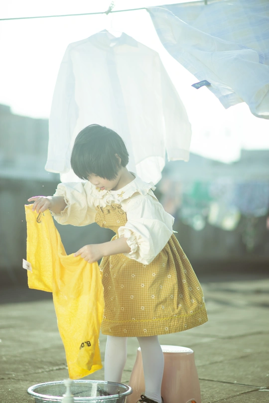 一个穿着黄色连衣裙的年轻女孩把伞放在一小碗洗好的衣服上