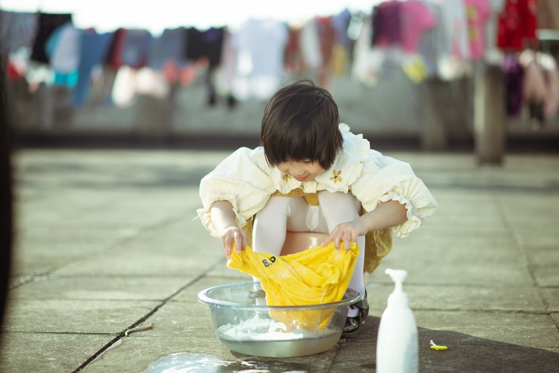 一个小女孩在人行道上洗衣服的黄色碗里玩耍