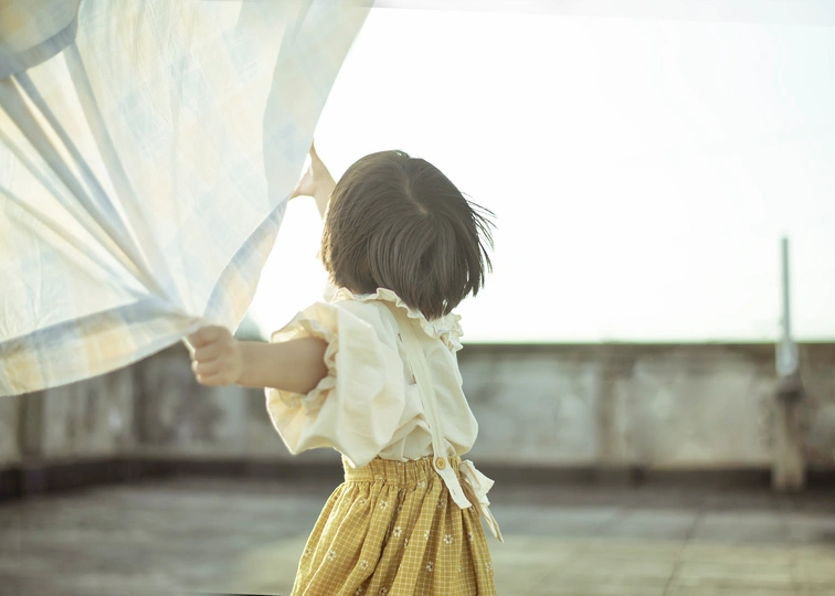 一个穿着黄色连衣裙的小女孩站在手提箱上打开窗帘