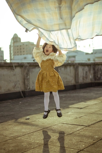 一个穿着黄色连衣裙的小女孩站在屋顶上 伞在空中飞舞