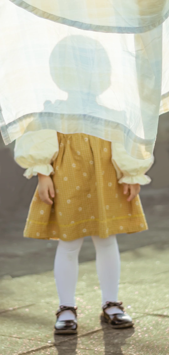 一个穿着黄色连衣裙、打着白色雨伞的小孩