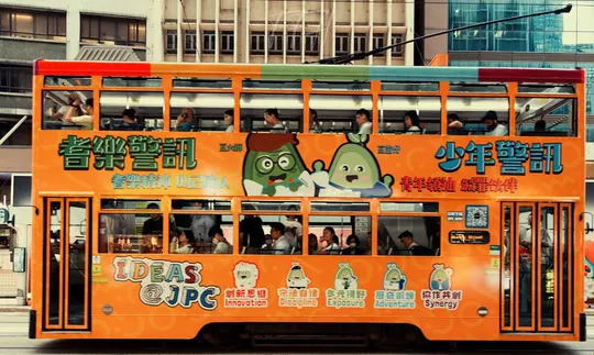 一辆橙色的双层公交车在城市街道上行驶 背景是建筑物。
