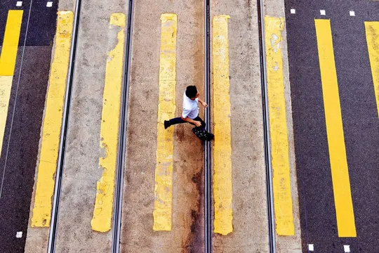 一个人坐在黄色的火车轨道上 人们穿过街道。