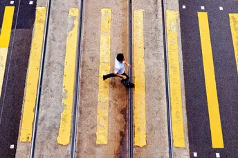 一个人坐在黄色的火车轨道上 人们穿过街道。