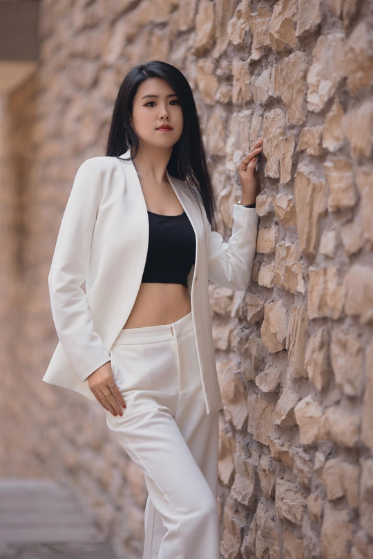 一位穿着黑色上衣和白色裤子的女人靠在街头石头墙上