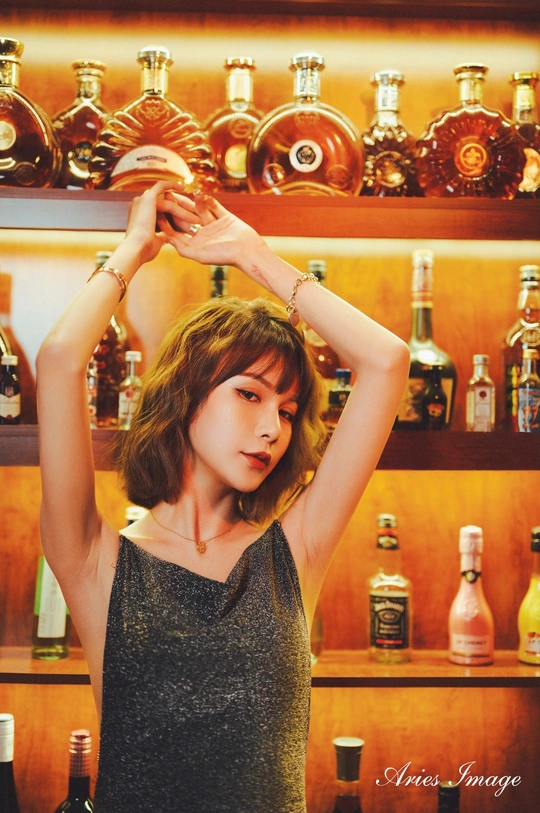 一位女子抱着头 站在酒吧前 酒吧里有瓶装酒。