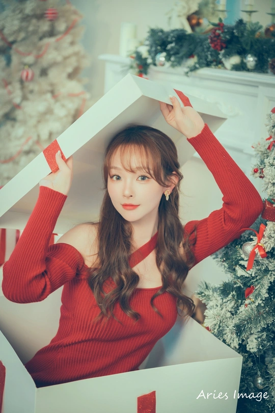 一位穿着红色毛衣的女人在圣诞树前用盒子顶在头上摆姿势