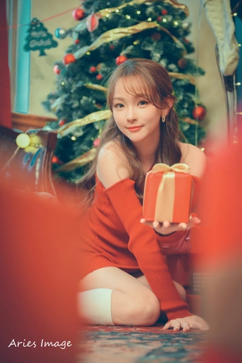 一位穿着红裙子的年轻女子在圣诞树前拿着礼物