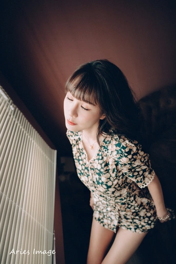 一位穿着连衣裙的年轻女子站在窗前 窗帘是关闭的。