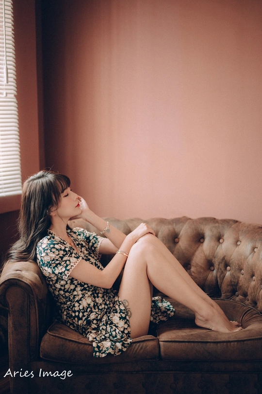 一个穿着连衣裙的年轻女子坐在沙发上 双腿交叉在窗户前。